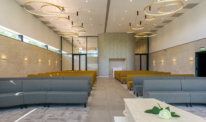 Grote zaal met houten uitvaartkist en vele rijen banken